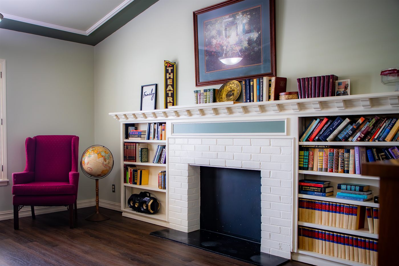 A quiet sitting room at Colonial Manor with a fireplace, bookshelves, and a comfortable wing chair