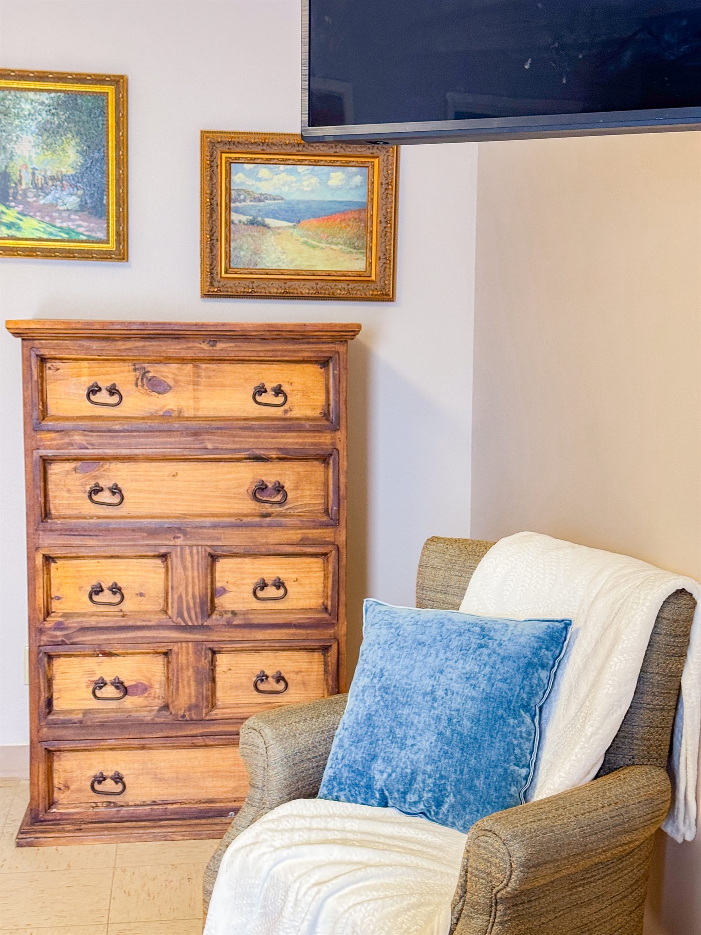 A resident's room corner with personal furnishings and framed art